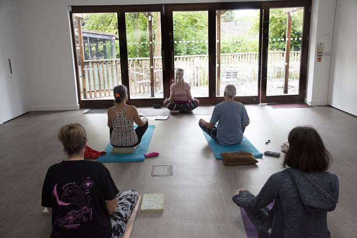Five women sit cross-legged on yoga mats