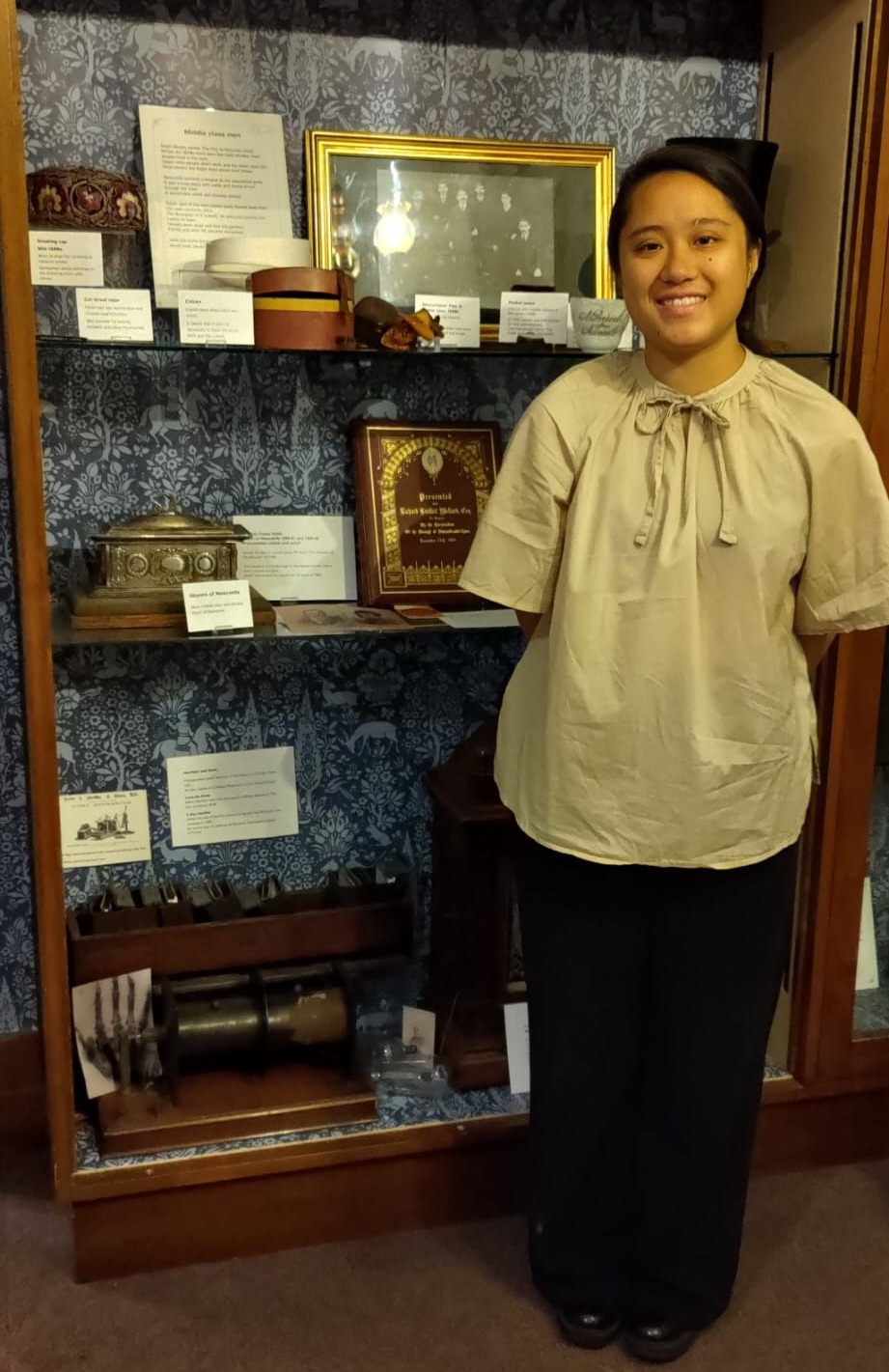 Bethany stands in front of an museum display case containing an old X-Ray Machine