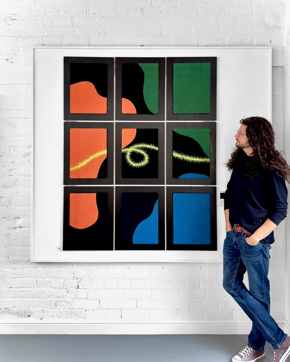 The image shows JPR Stitch standing next to a 9 panel colourful textile artwork.