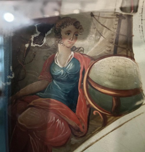 A close up of a painted clock face showing a seated woman looking at a globe