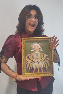 A smiling person holds an embroidery of a Tudor Queen in a gold frame