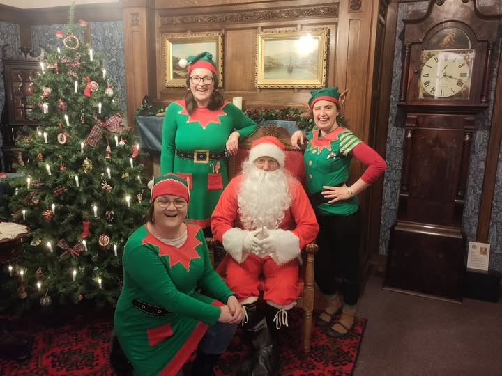 Santa and elves at the Brampton Museum, standing in the Victorian Parlour in front of a decorated Christmas tree