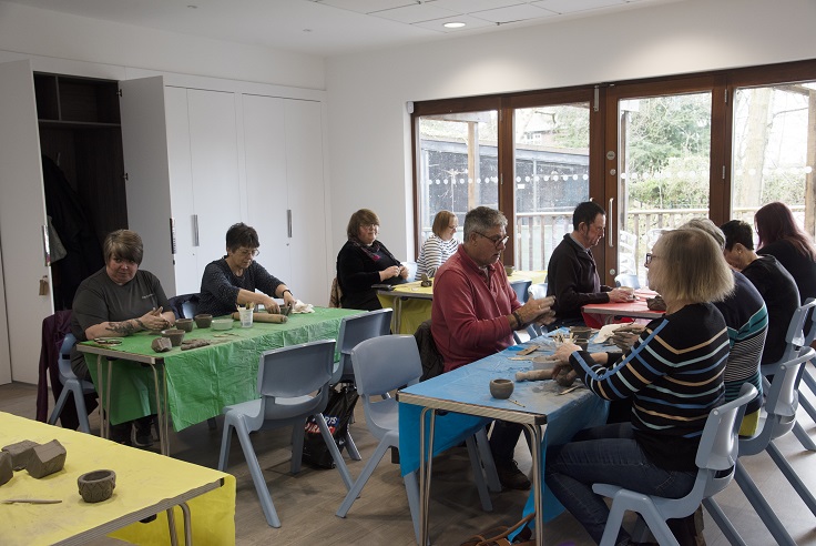 People handle clay seated at tables