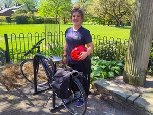 A smiling woman with a bike and helmet next to a bicycle rack