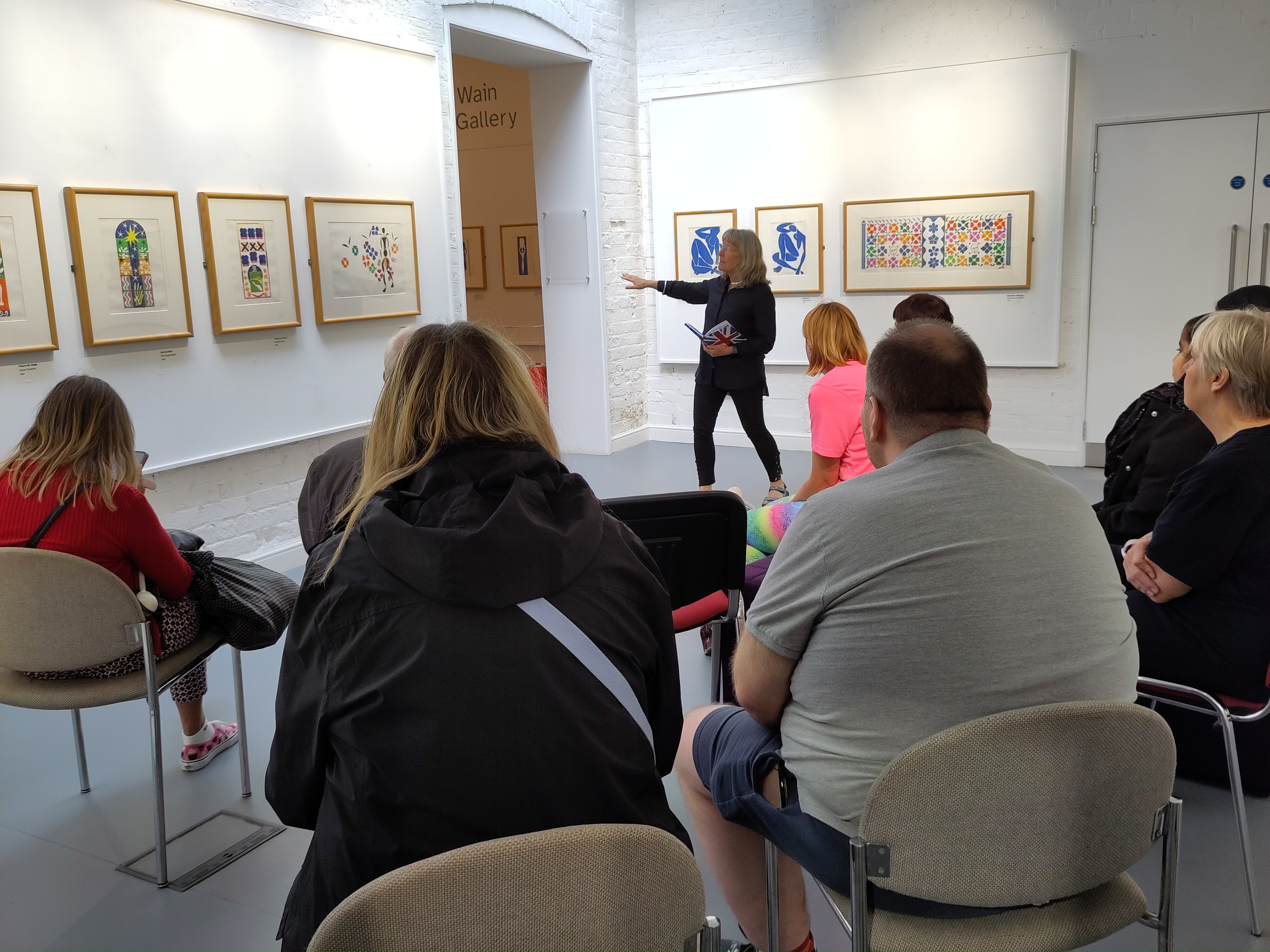 A woman points at bright artwork on a white wall