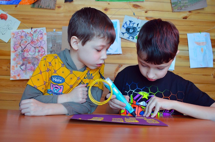 Two children lean over a table doing a craft activity