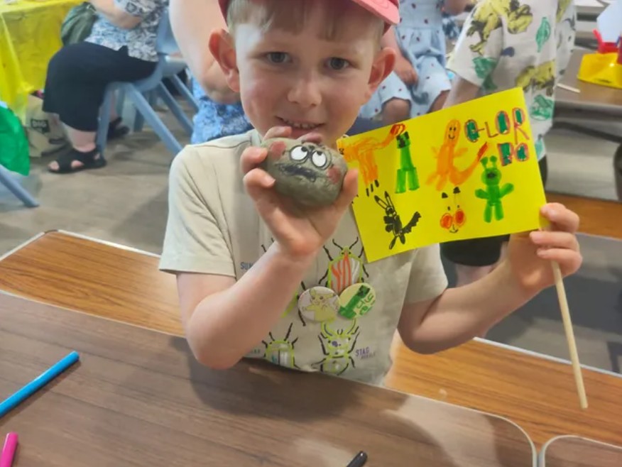 A child holds a painted rock with googly eyes and a painted flag.
