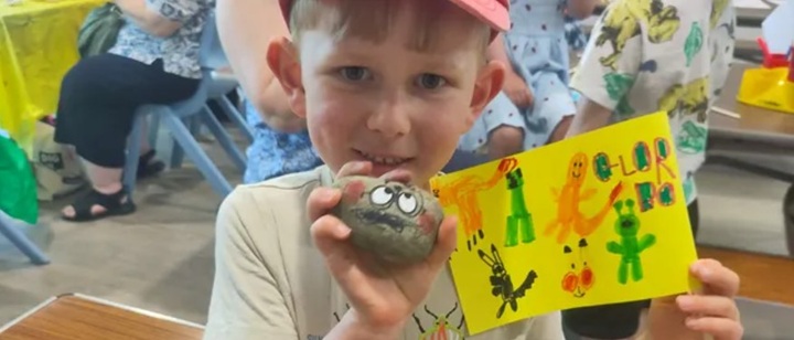 A child holds a painted rock with googly eyes and a painted flag.