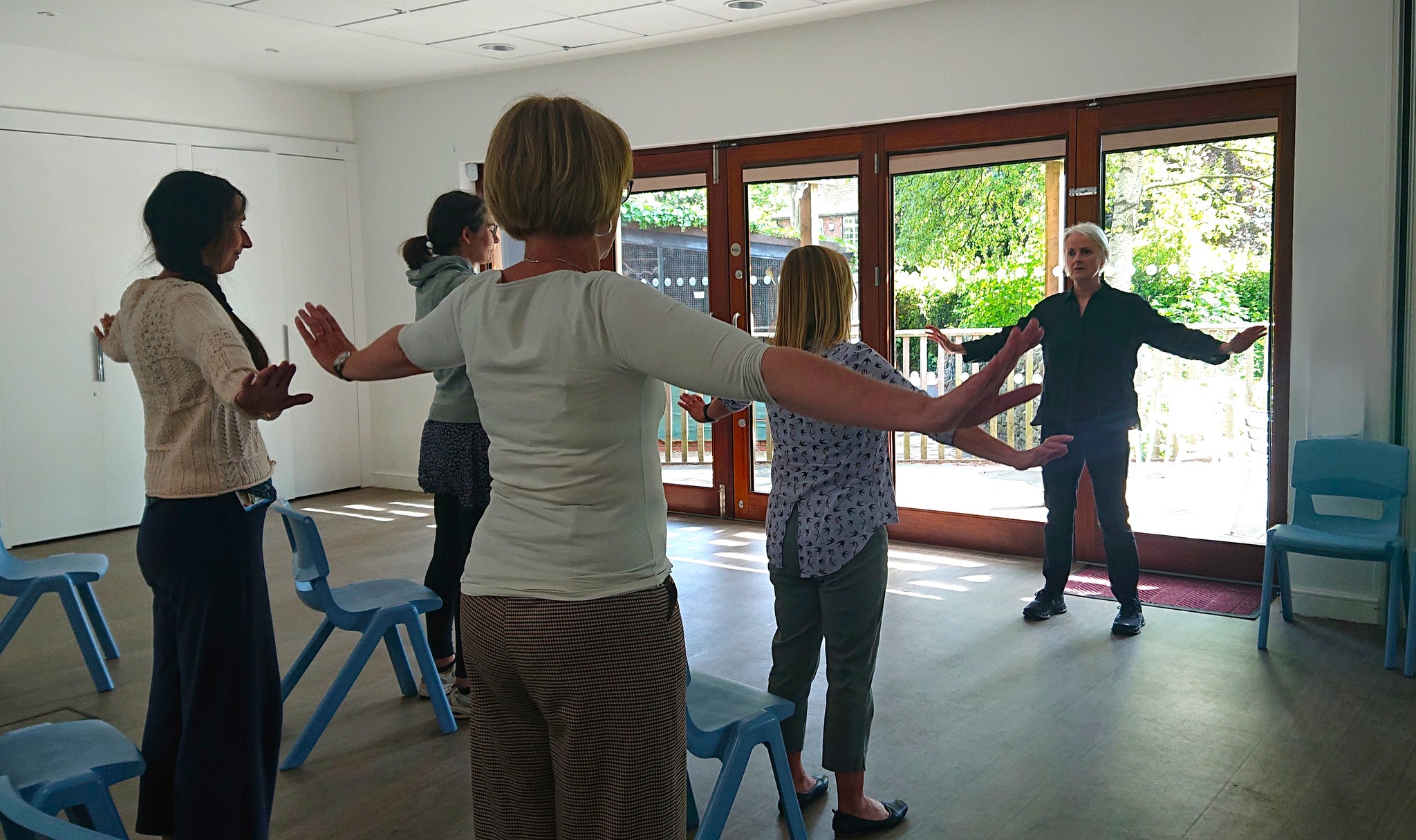 A standing group of people raising their arms with an instructor at the front of the room