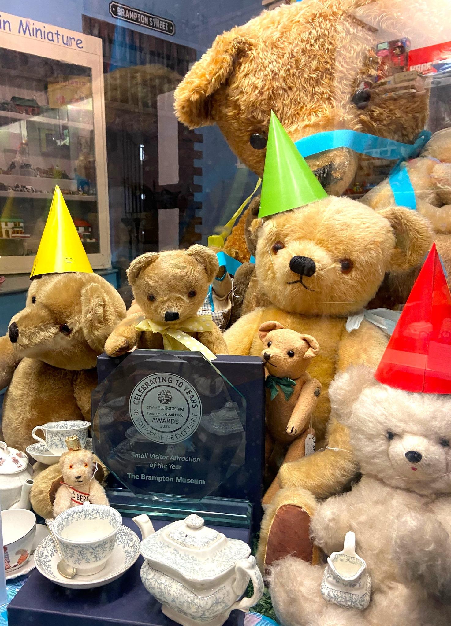 A glass display case full of old teddy bears in party hats surrounding a glass award
