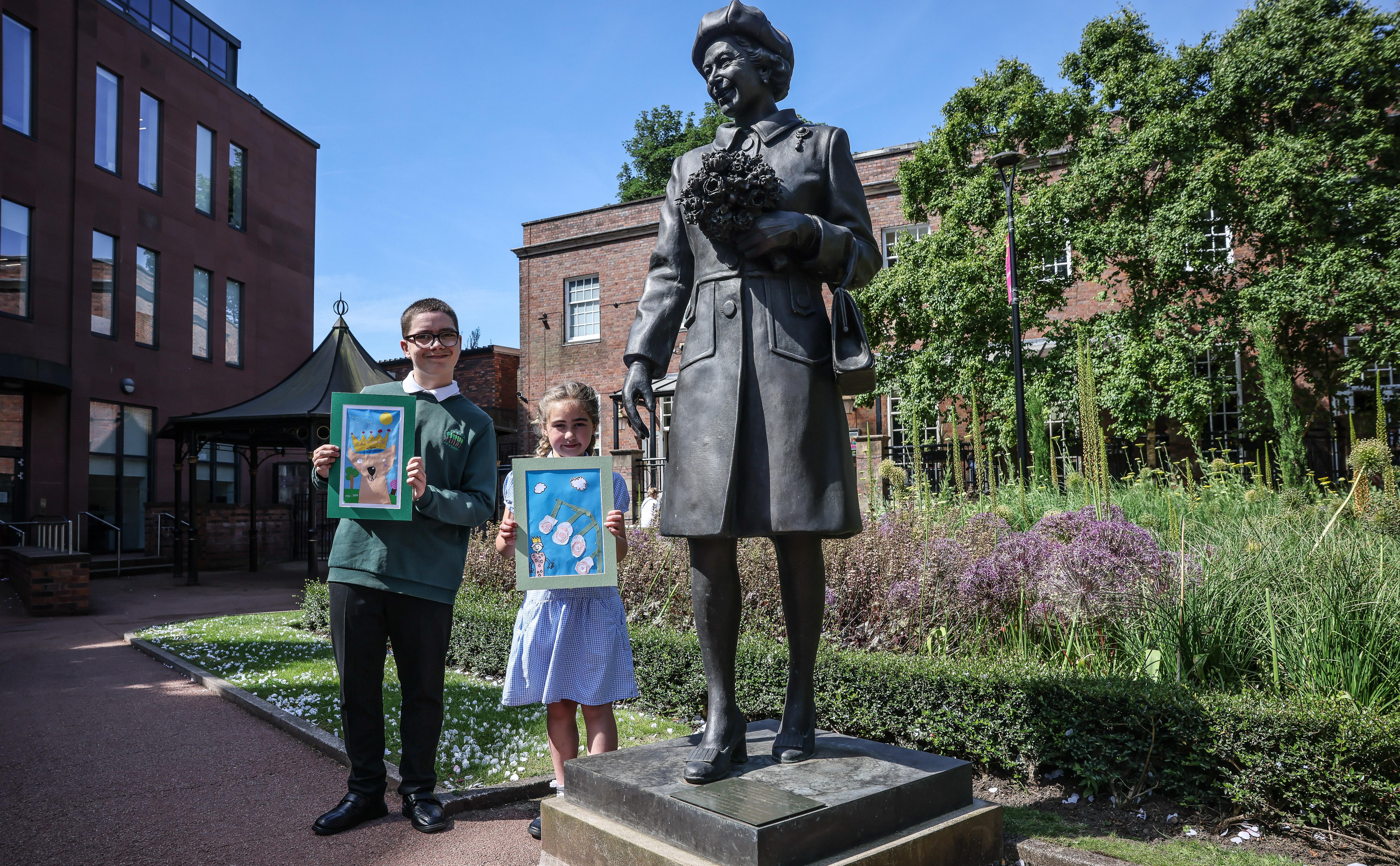 Young Ethan and Ava with their winning paintings standing next to the landmark Queen Elizabeth II statue in Queens Gardens.